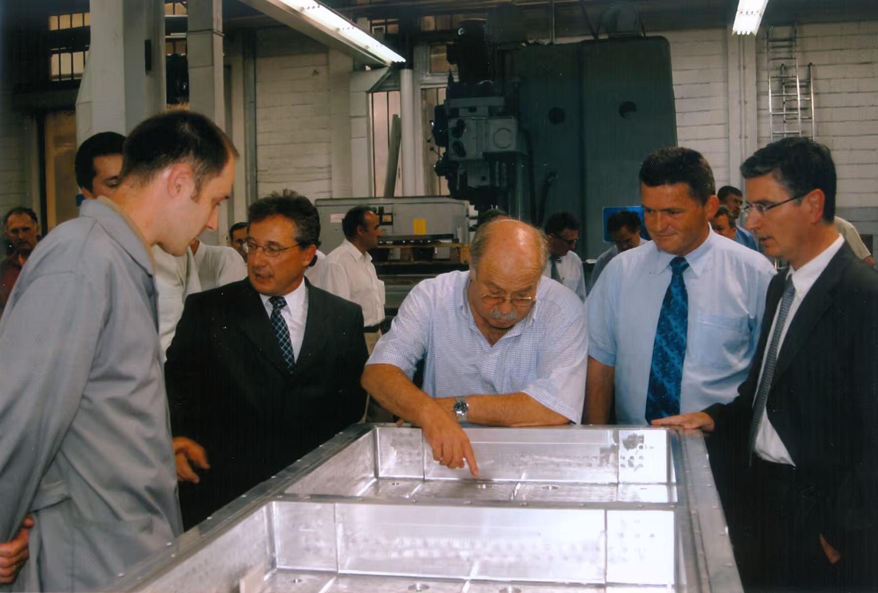 Staff and visitors in the workshop examining a large polished aluminium tool plate, one of them pointing out a detail.