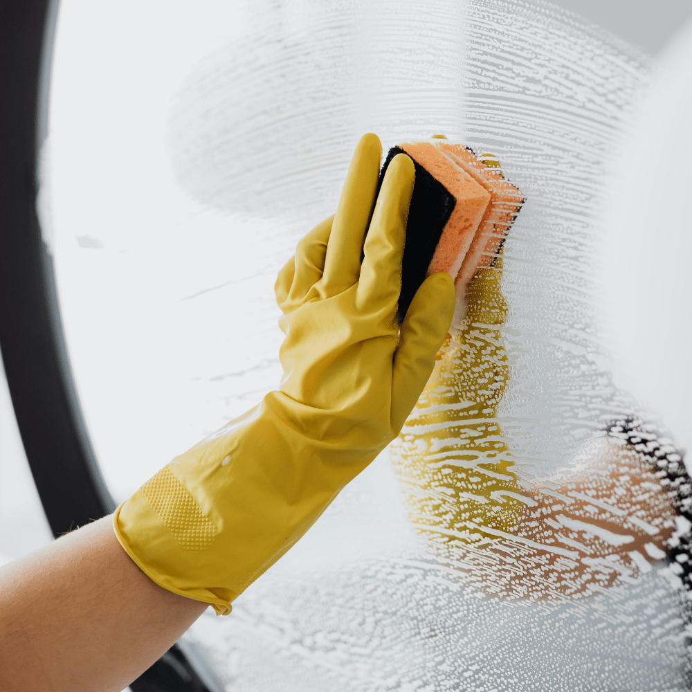 Reinigungskraft wischt mit Schutzhandschuh und Tuch eine Wand ab