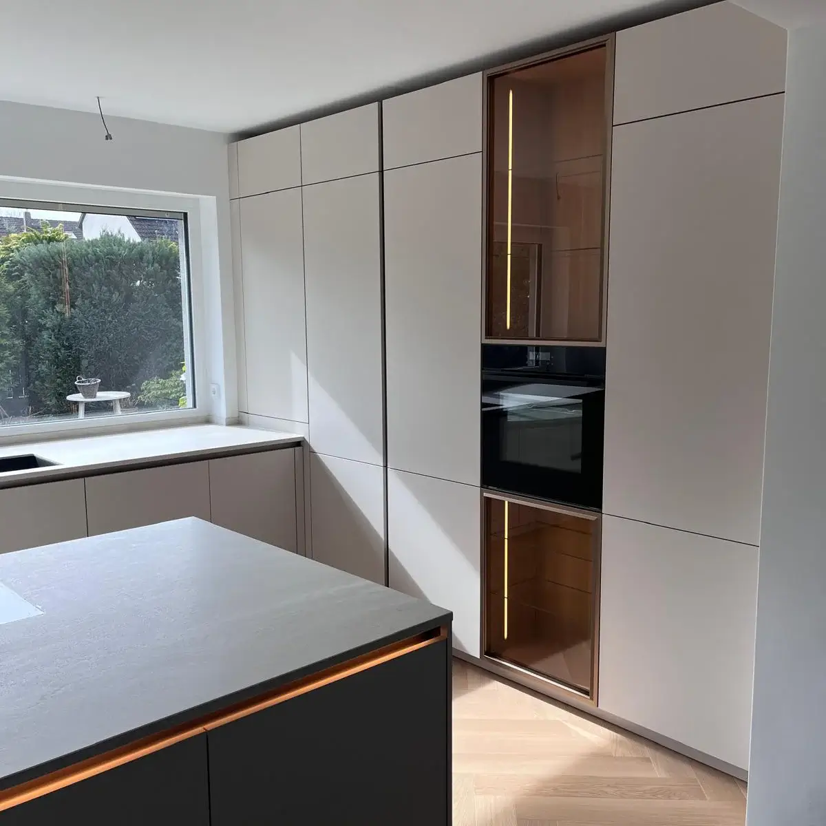 Moderne Küche mit mattschwarzer Insel, hellen Schränken und großem Fenster zum Garten.