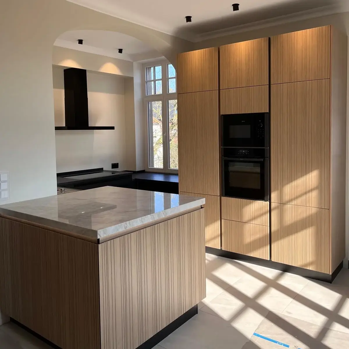 Moderne Küche mit Holzschränken, Kücheninsel mit Marmorplatte und schwarzen Geräten bei Tageslicht.