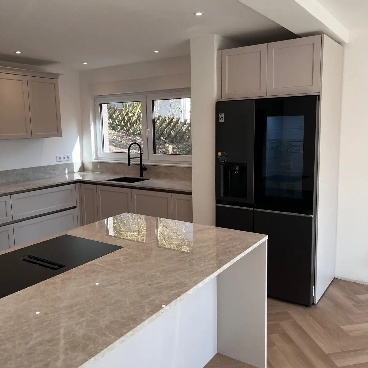 Moderne Küche mit schwarzem Kühlschrank, Marmorarbeitsplatte und Waschbecken unter dem Fenster.