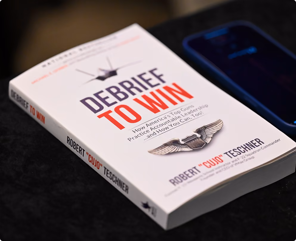 Copy of Debrief to Win, the VMax Group book on no-blame debriefs and team accountability, on a desk