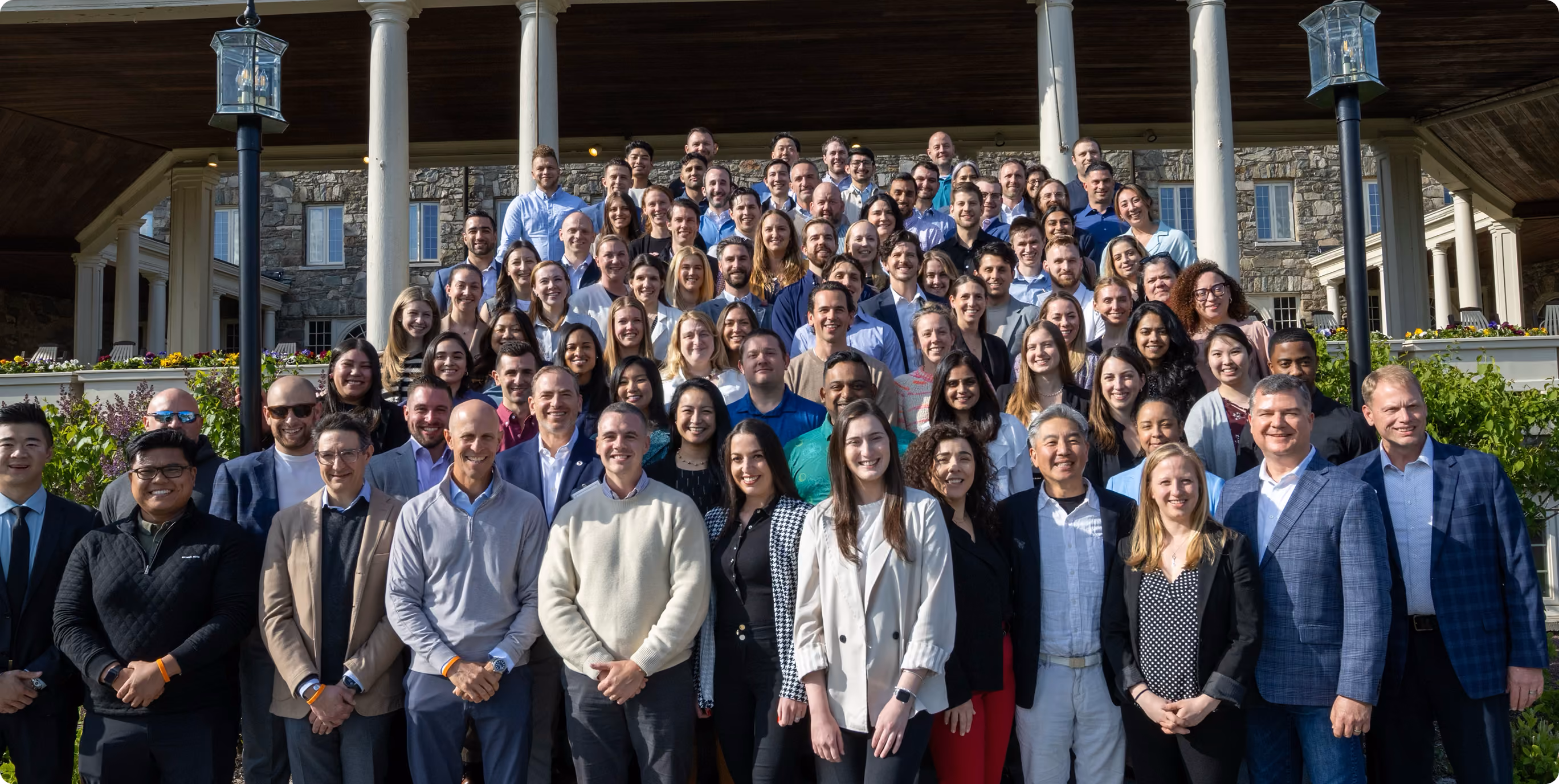 Large group photo of a client team with VMax Group instructors on the steps of a conference venue