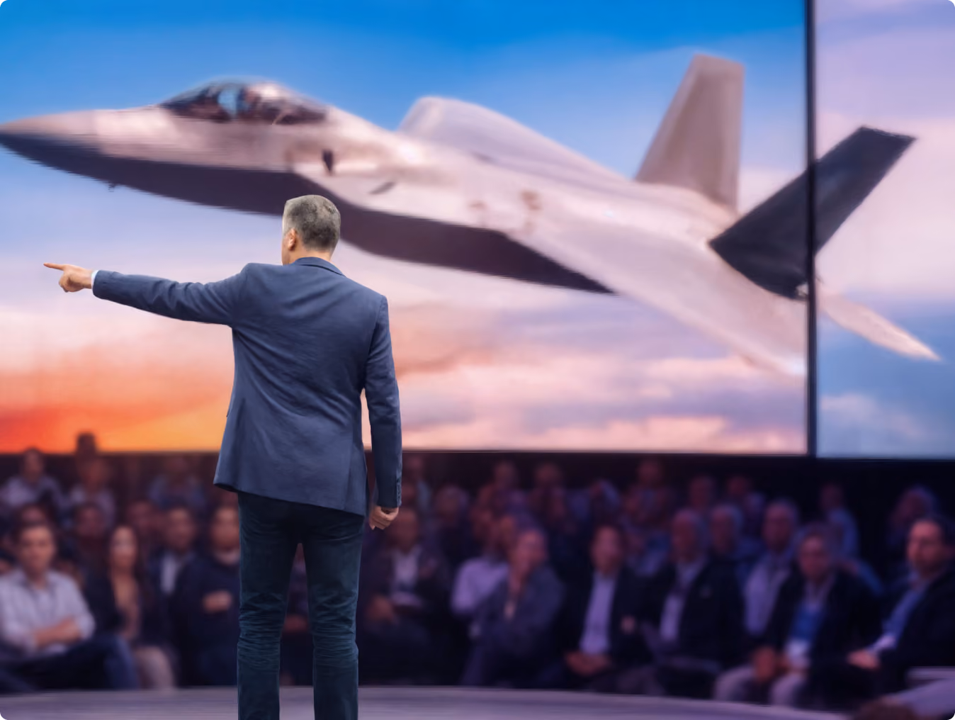 Robert "Cujo" Teschner on stage explaining the VMax Group team operating system with a fighter jet on the screen