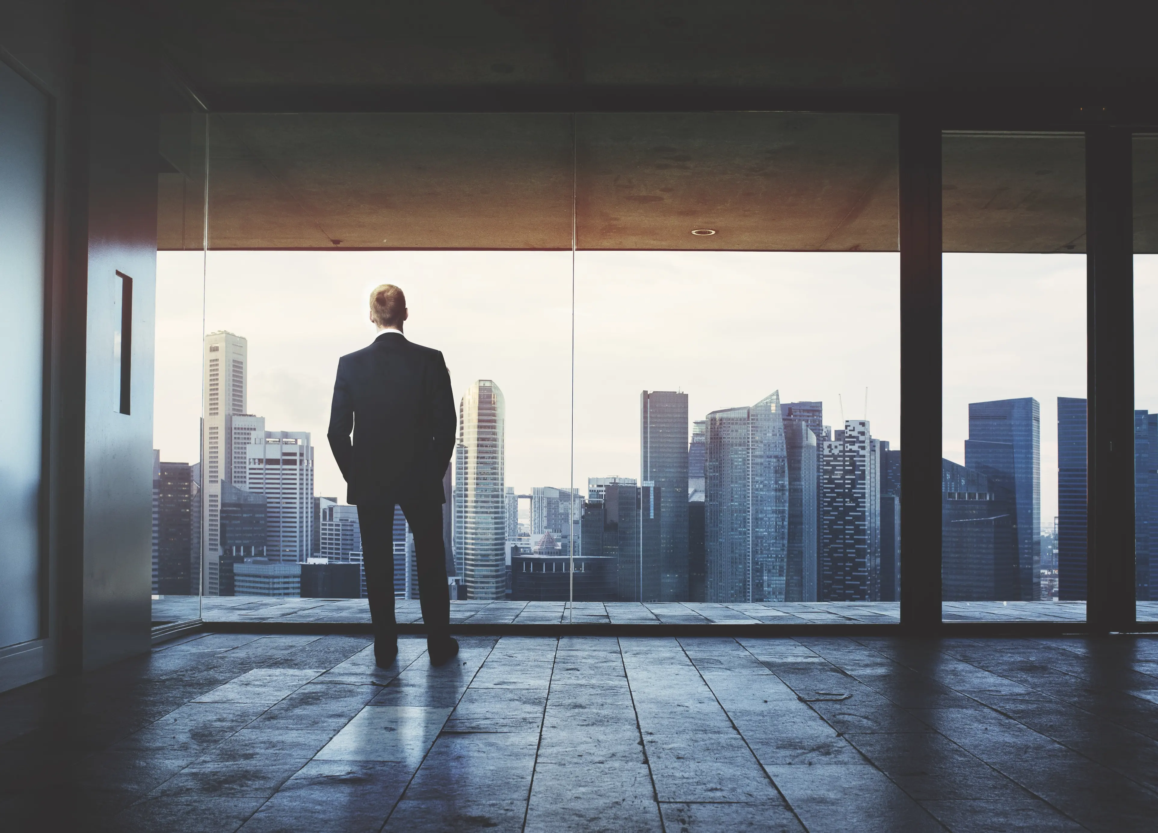 A man in a suit looking out over a city skyline from a high-rise window