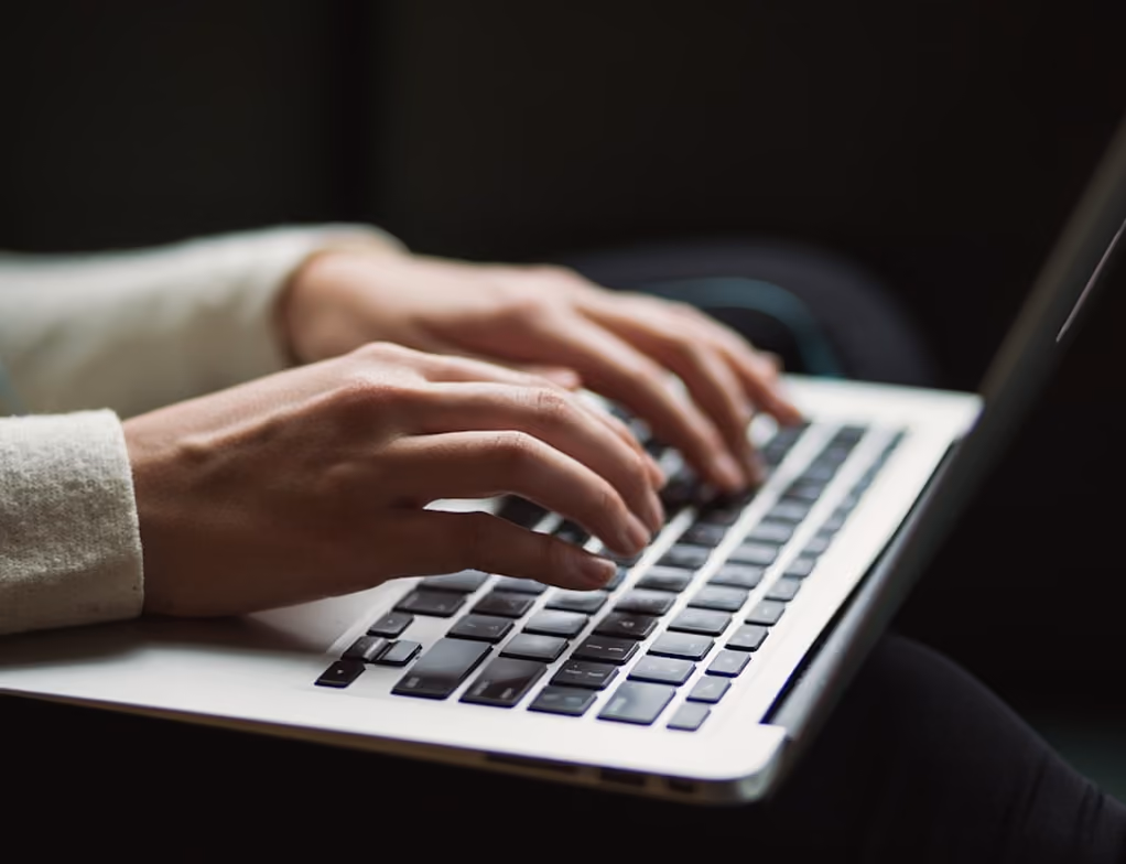Mains tapant sur le clavier d'un ordinateur portable avec un fond sombre.