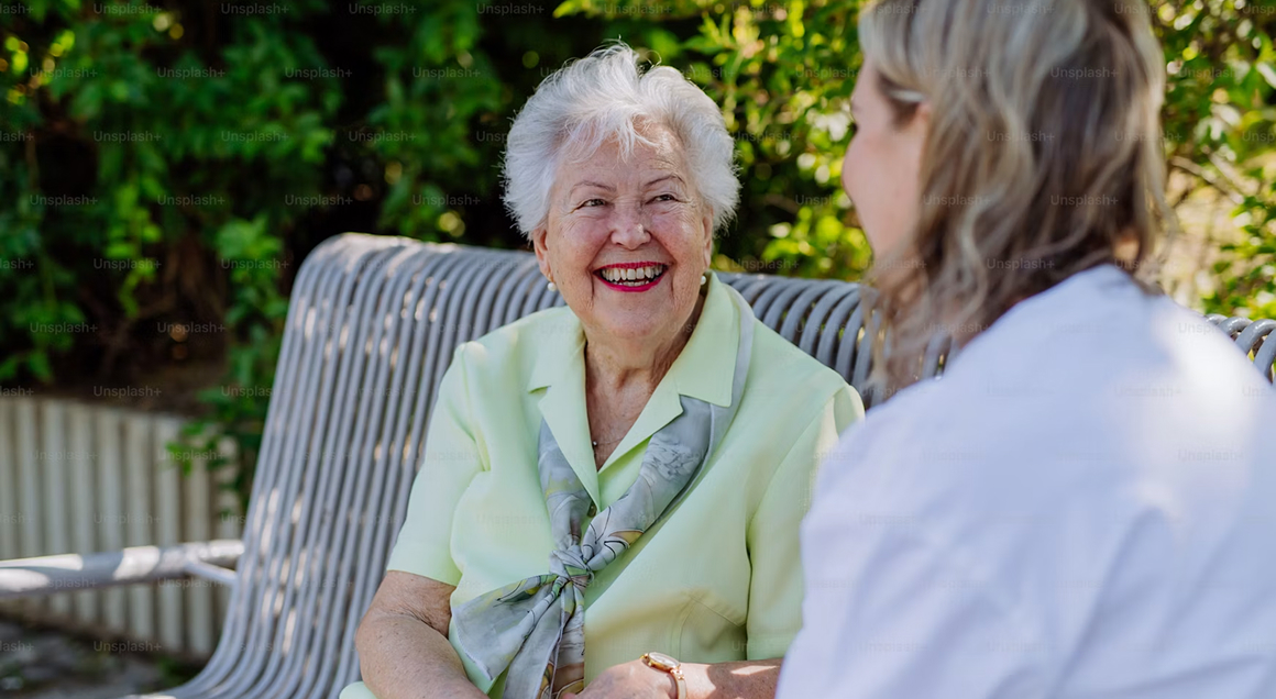 Ältere Frau im Gespräch mit einer Pflegekraft im Garten