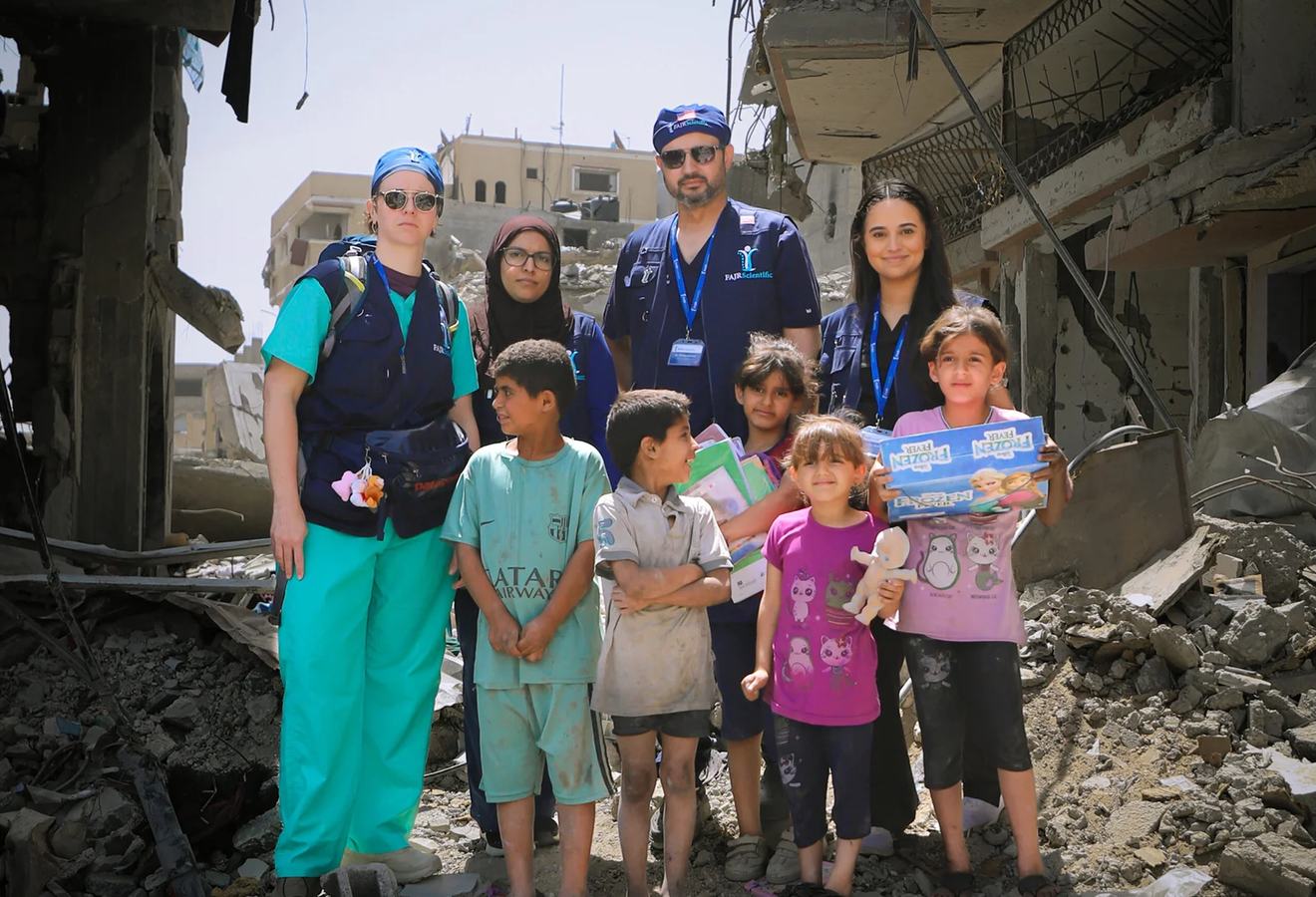 A FAJR medical team standing with children among destroyed buildings in Gaza.