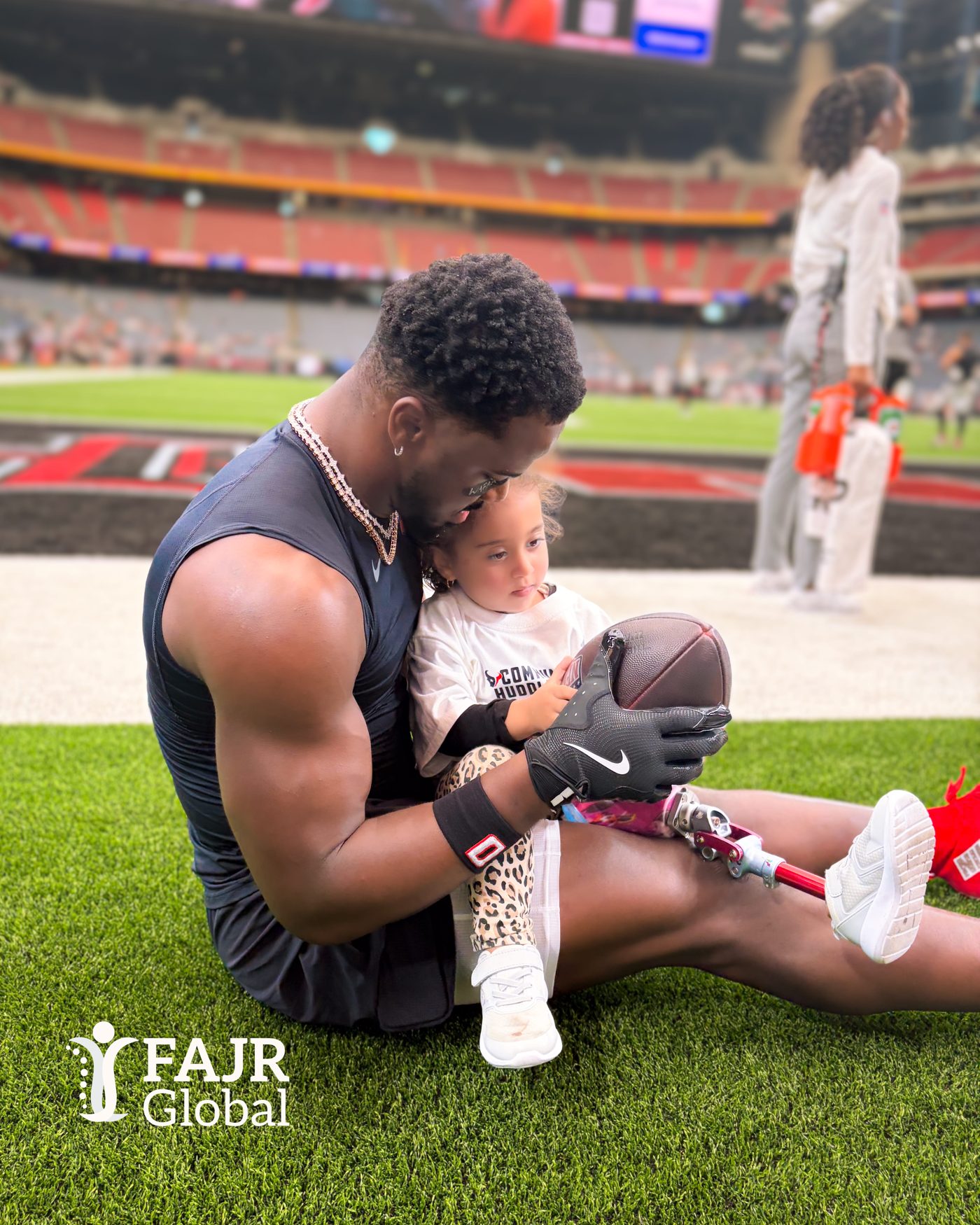 A Houston Texans player shares a football with a young girl with a prosthetic leg on the field