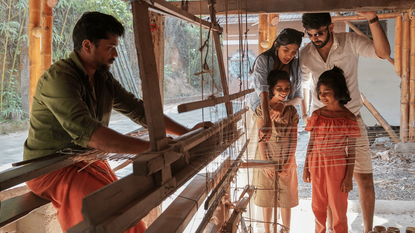 A weaver at a wooden handloom under a thatch shelter