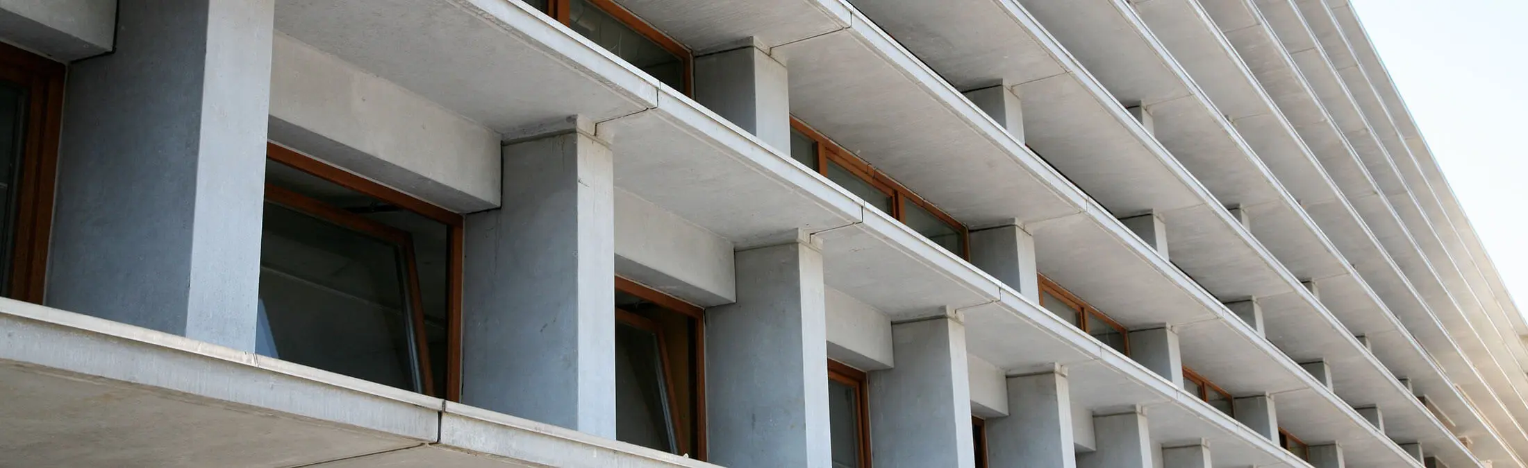 Moderne gebouwgevel met meerdere verdiepingen en uitkragende betonnen balkons met ramen tussen betonpilaren.