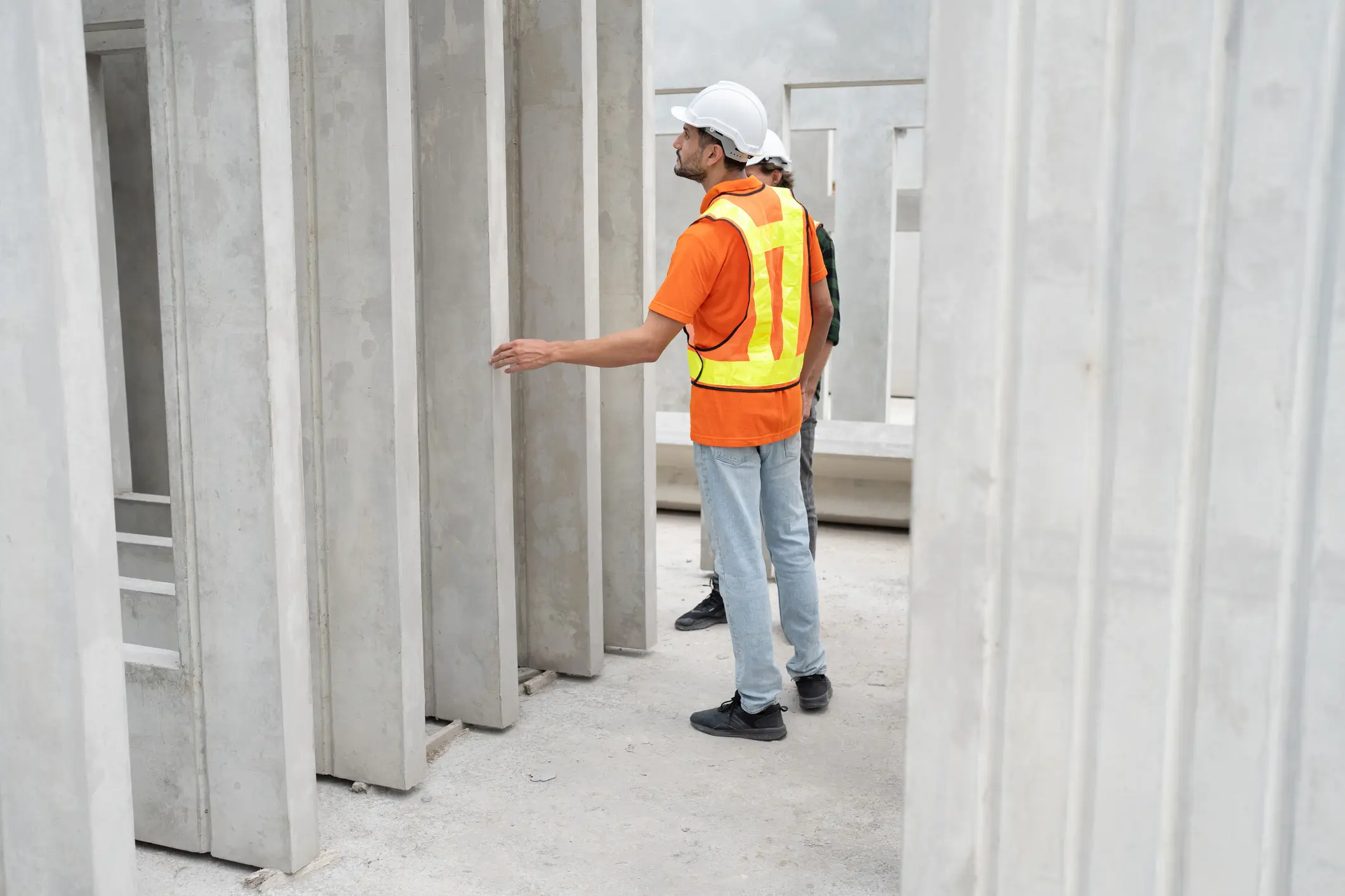 Twee bouwvakkers met veiligheidsharnassen en helmen onderzoeken en inspecteren staanbetonnen panelen op een bouwplaats.