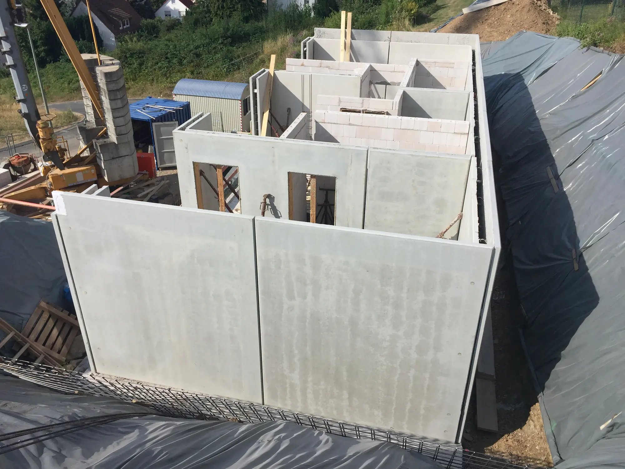 Een betonnen bouwstructuur in aanbouw met verschillende scheidingsmuren op een bouwterrein, omgeven door bouwmateriaal en een hijskraan.