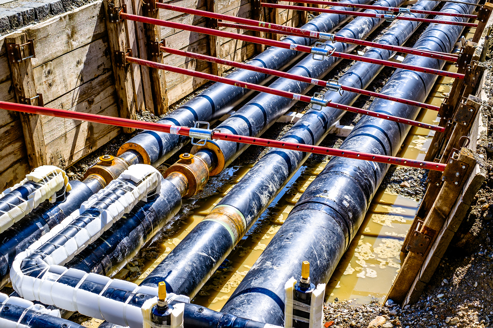 Large black pipes laid in a shored trench during underground installation.