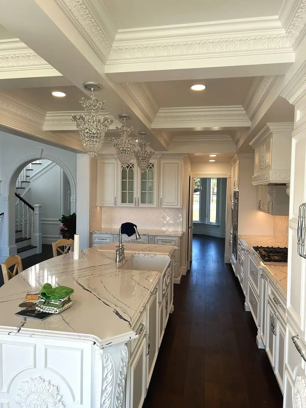 Interior of a spacious kitchen with ornate white cabinetry, a marble countertop island, and crystal chandeliers