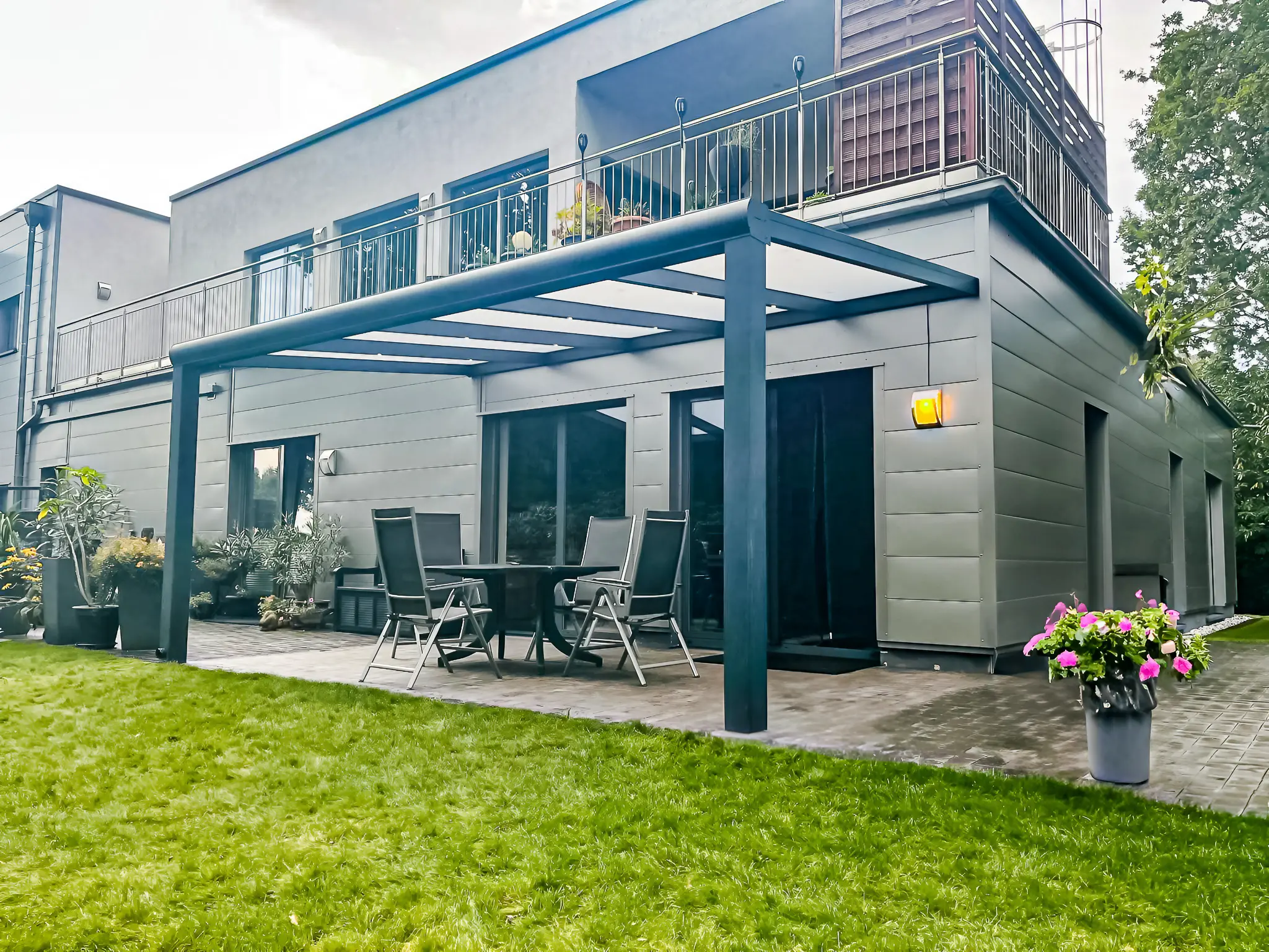 Moderne Terrasse mit Überdachung, Gartenmöbeln und blühenden Pflanzen