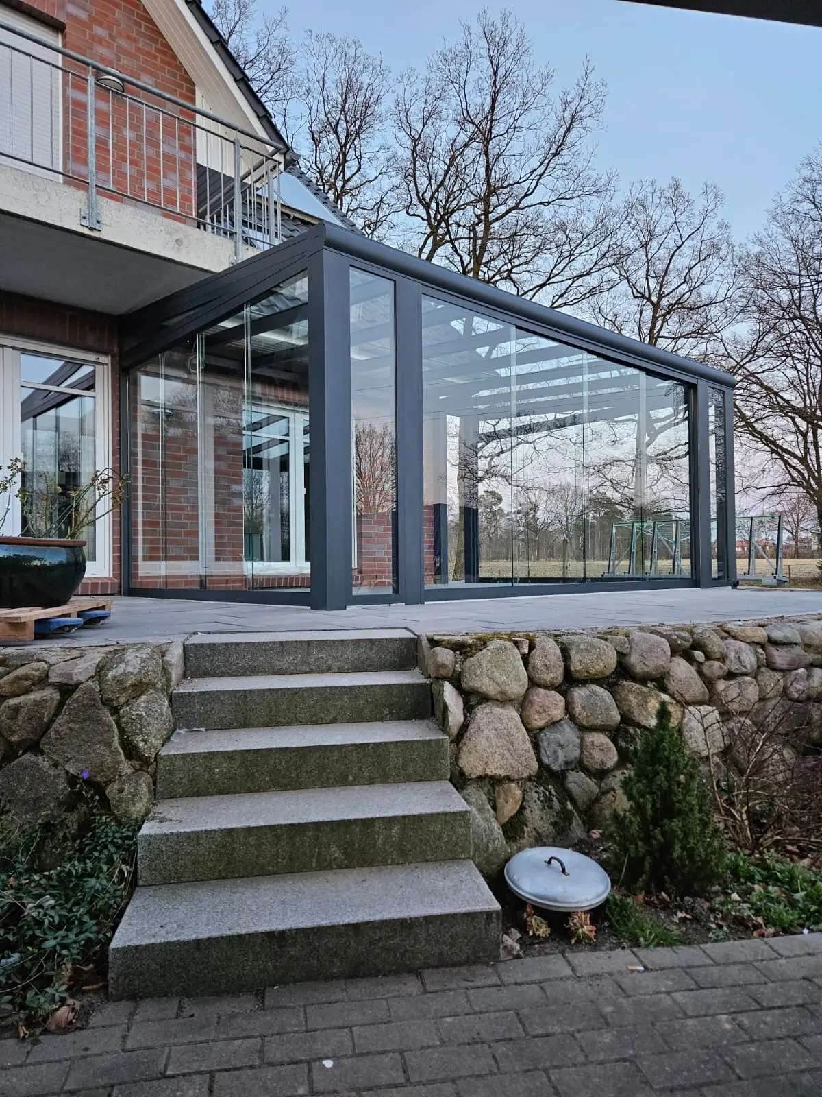 Moderner Wintergarten mit Glaswänden und Natursteintreppe an Ziegelhaus