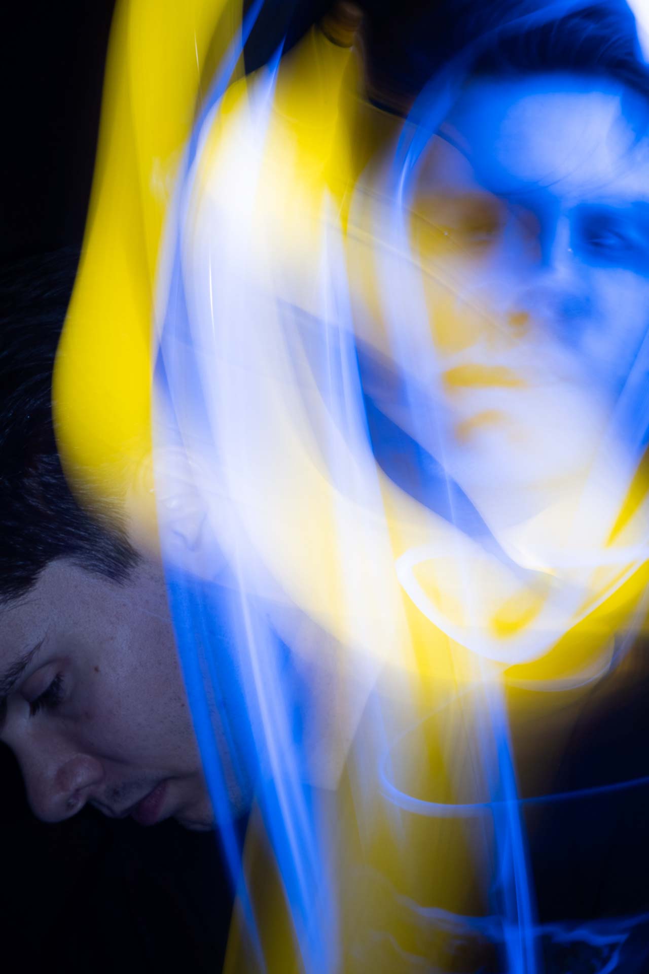 Blurred double portrait of a person with blue and yellow light trails creating an abstract effect.