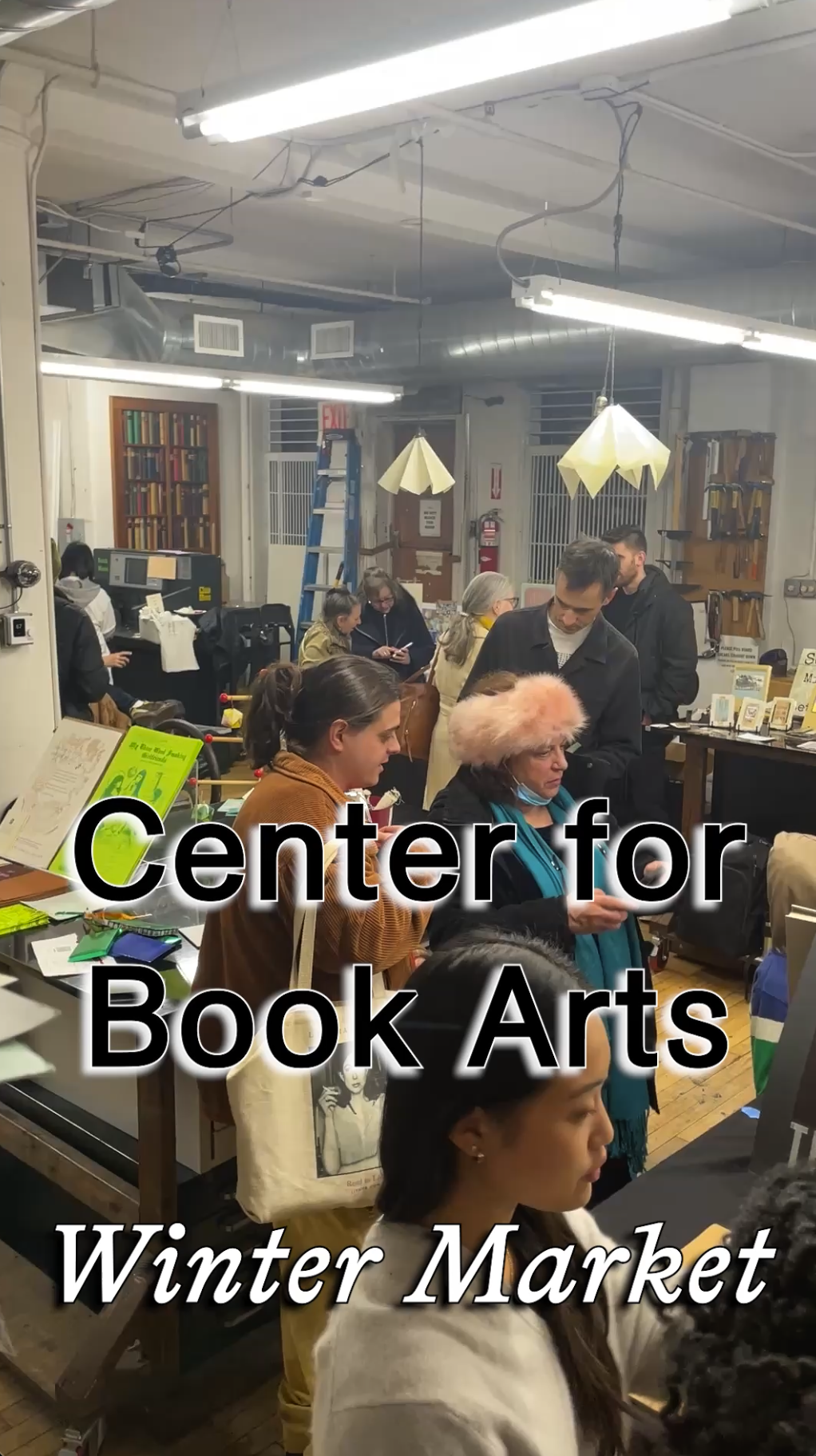 Indoor scene at a busy winter market event hosted by the Center for Book Arts, showing people browsing tables with books and art materials under bright fluorescent lights.