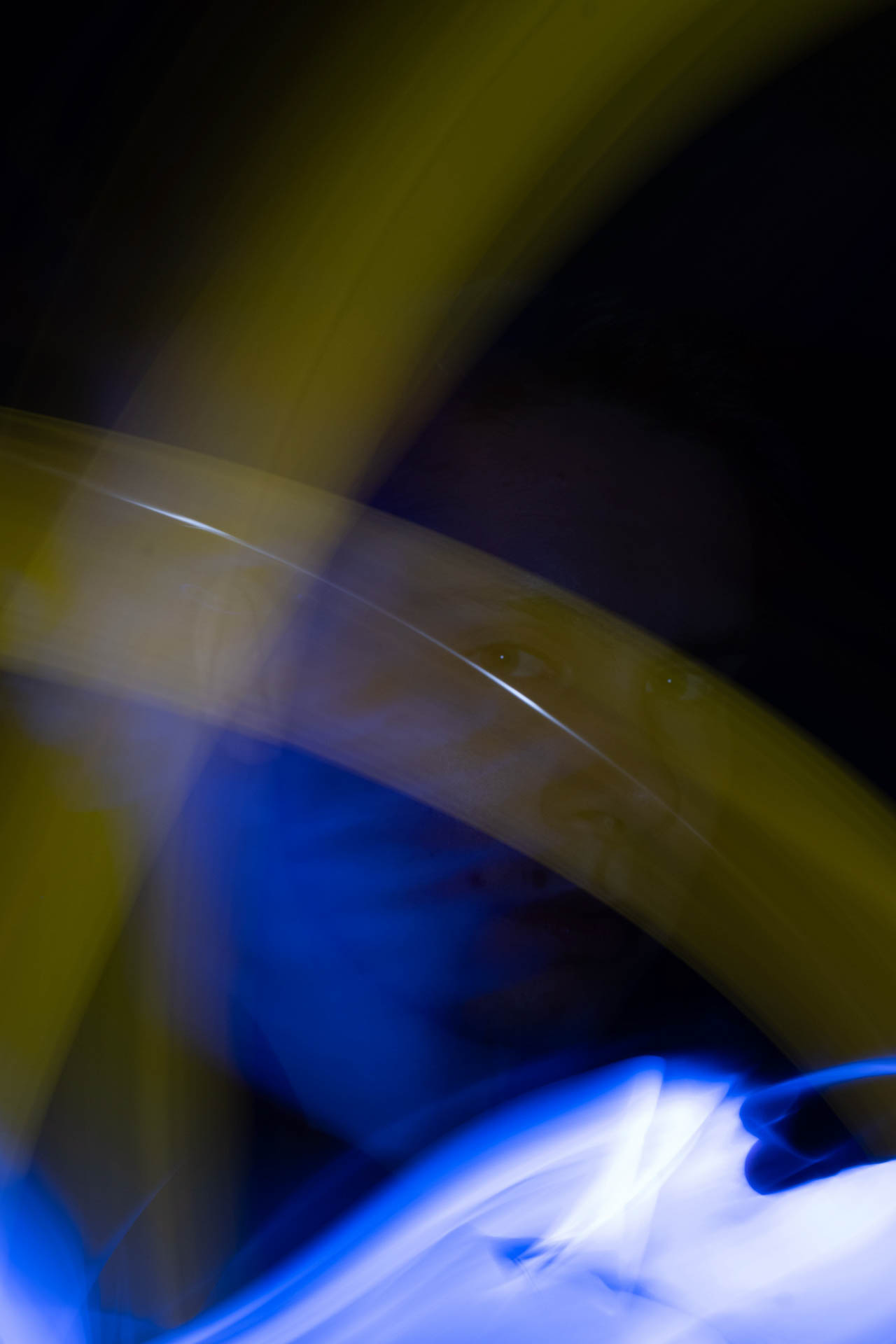 Portrait of a person's face partially visible behind swirling blue and yellow light trails on a black background.