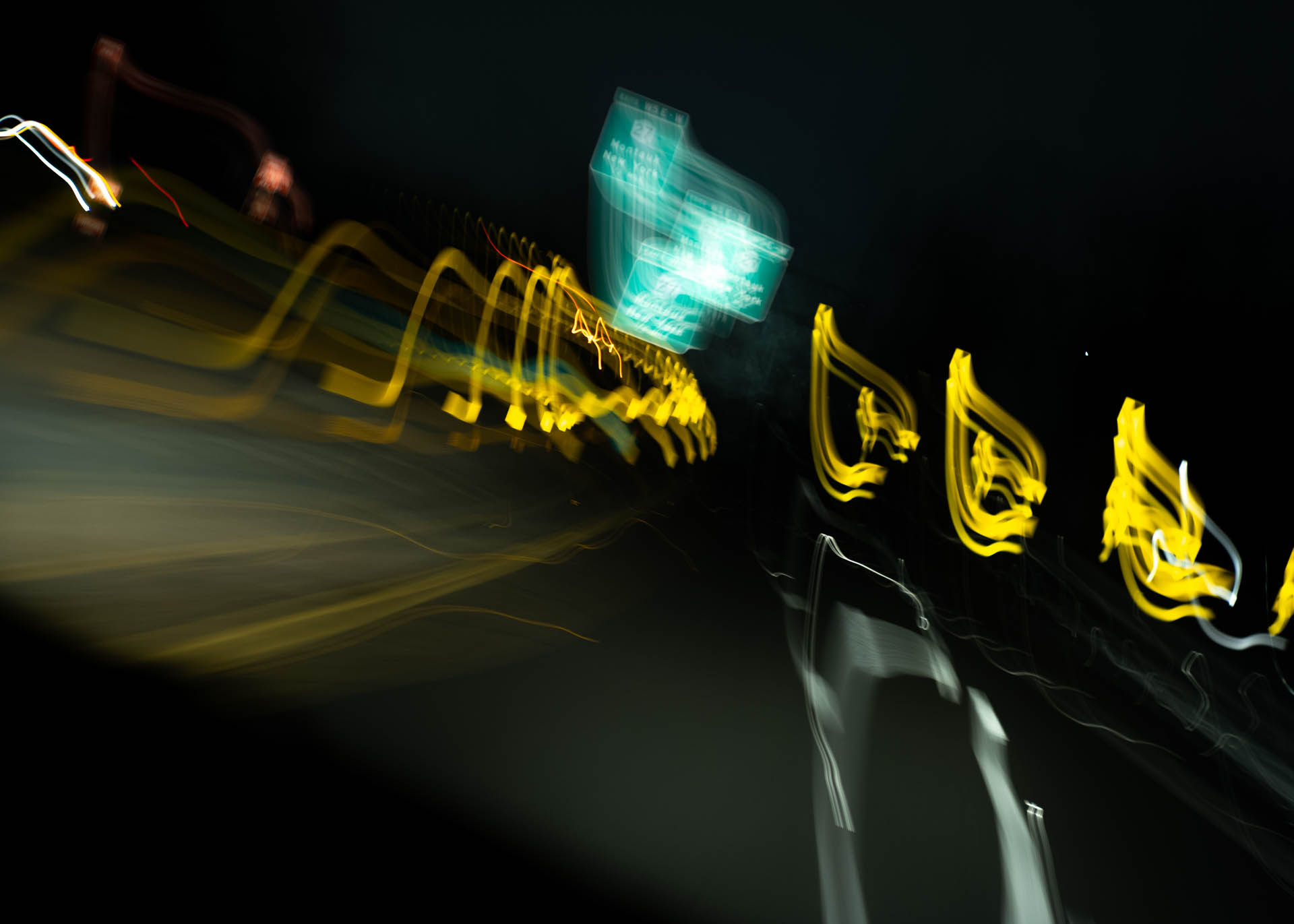 Blurred nighttime road scene with streaks of yellow and white lights and a green highway sign, creating abstract light trails.