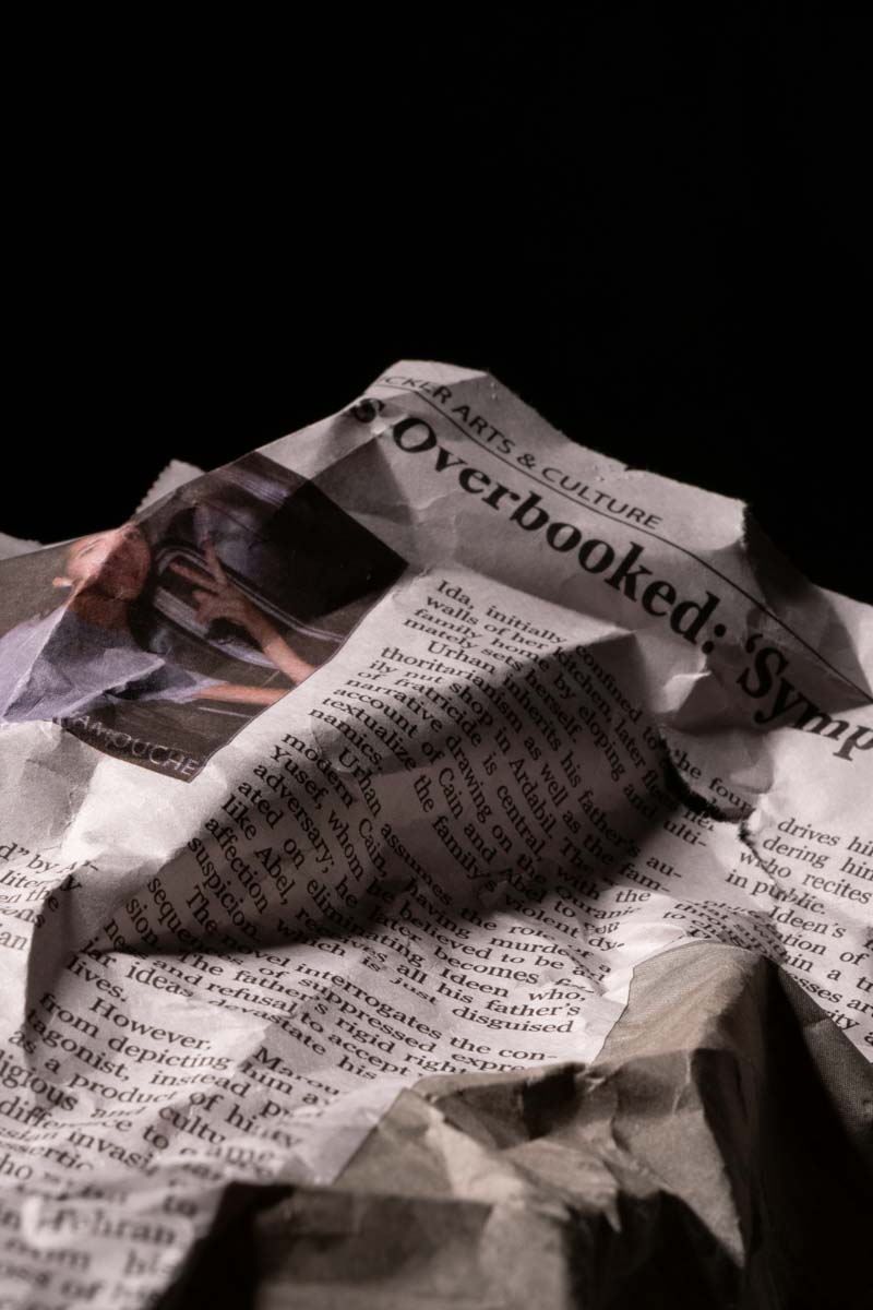 Crumpled newspaper page with a headline about arts and culture titled 'Overbooked'.