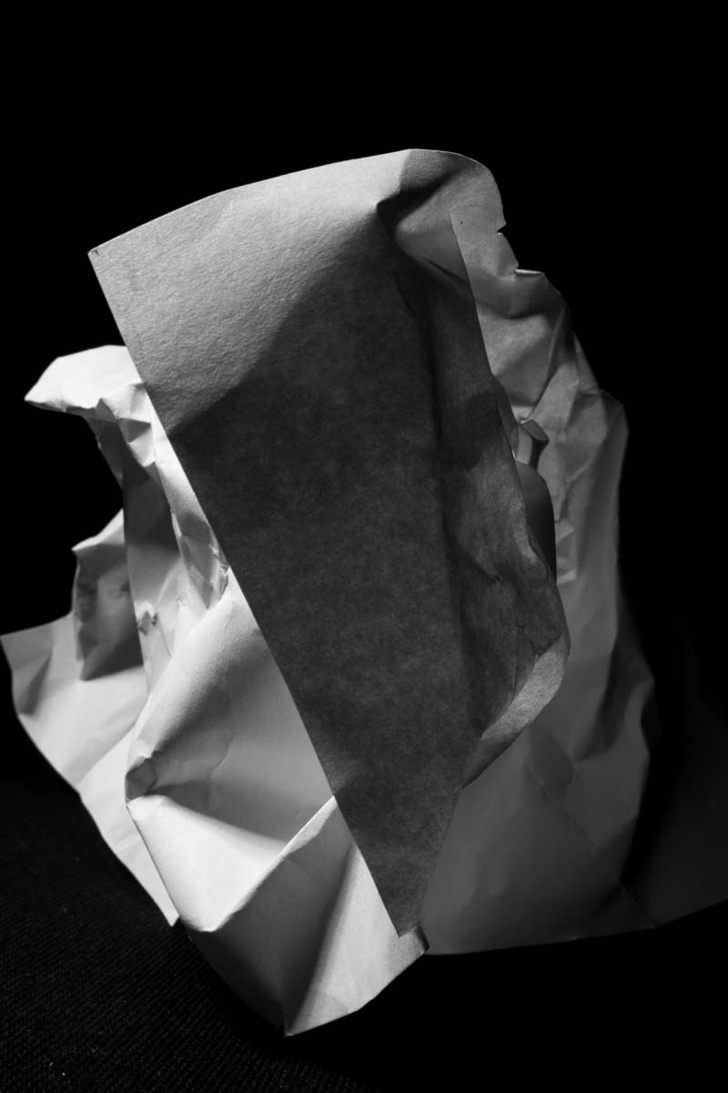 Black and white photo of a crumpled sheet of paper on a dark surface.