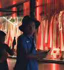 Person wearing a blue shirt and black hat in a dimly lit room with red and white striped curtains and reflective surfaces.