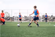 Young boys playing soccer on a green field with a goal net and houses in the background.