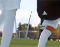 Close-up of two people playing soccer on a grass field, focusing on their legs and a soccer ball.