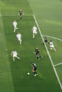 Soccer match moment with a player in blue about to kick the ball near the goal while several defenders and the goalkeeper in white attempt to block.