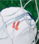 Close-up of a white soccer ball partially caught in the net of a goal with green grass in the background.