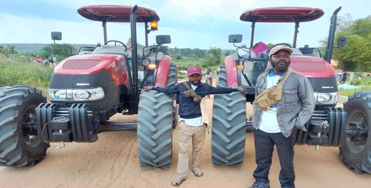Deux tracteurs rouges neufs garés sur une piste de terre, avec deux membres de l'équipe debout devant.
