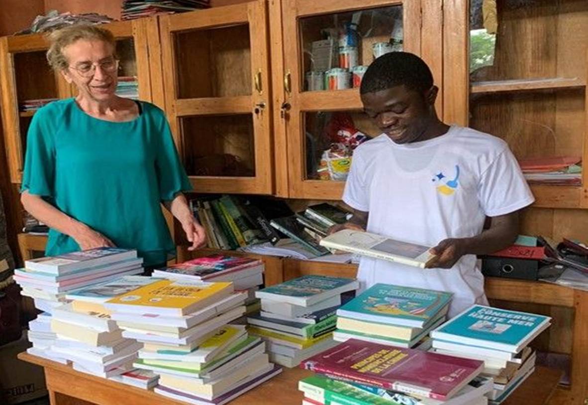 Une enseignante et un étudiant trient une pile de livres devant les étagères d’une bibliothèque.