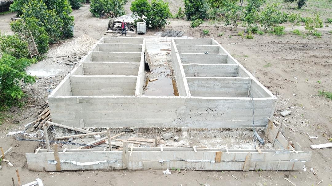 Structure de bassins en béton en cours de construction, sur un terrain sablonneux.