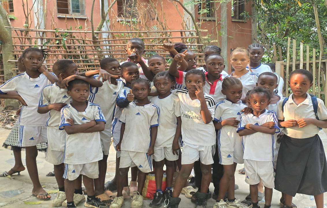 Groupe d’enfants en uniforme blanc devant un bâtiment en brique.