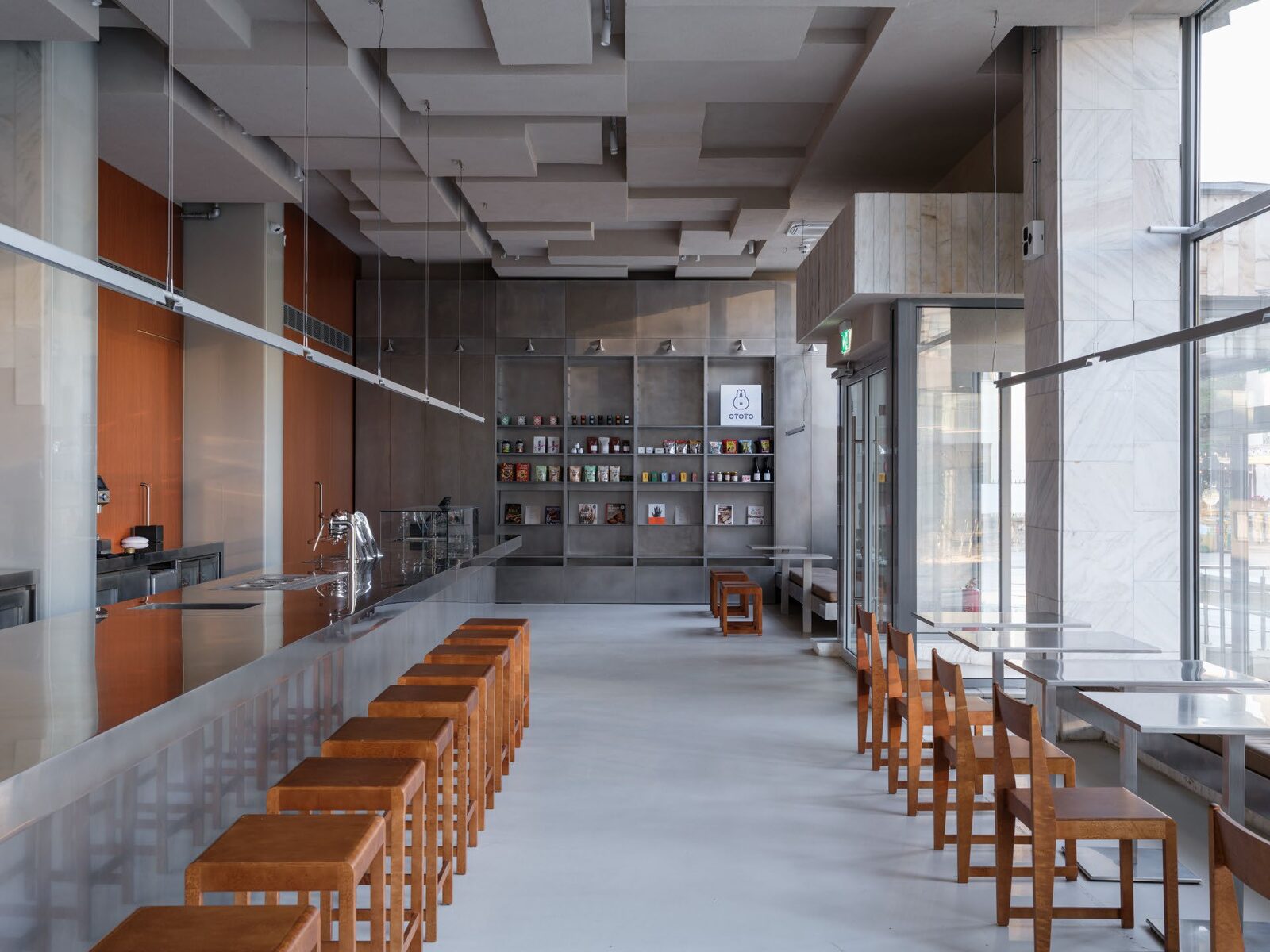 Eggcetera dining hall with a long brushed stainless steel counter, timber stools and a steel shelving wall at the far end