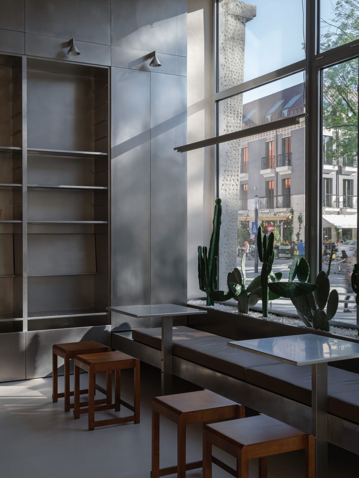 Stainless steel window bar with timber stools and full-height steel shelving in a café