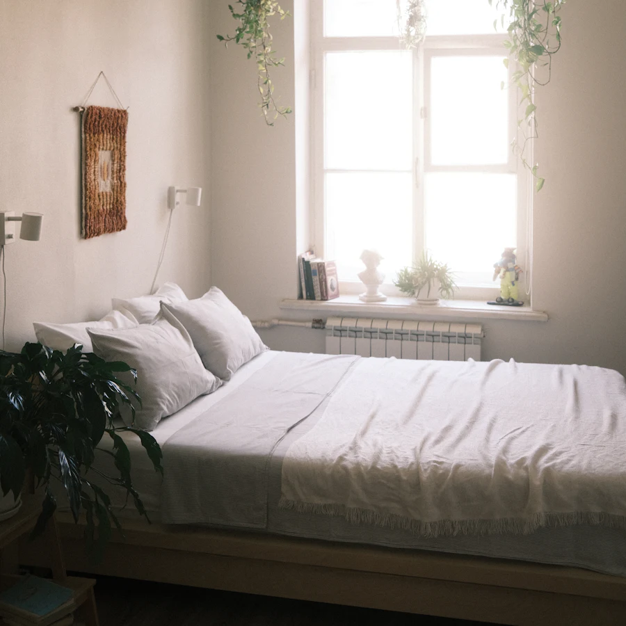 Chambre lumineuse avec lit en linge blanc et plantes à la fenêtre
