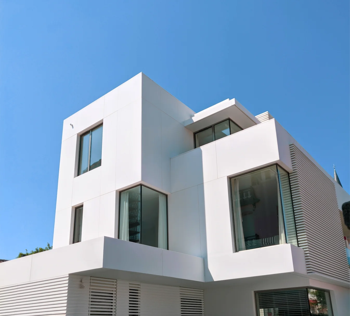 Maison contemporaine blanche aux grandes baies vitrées noires, sous un ciel bleu