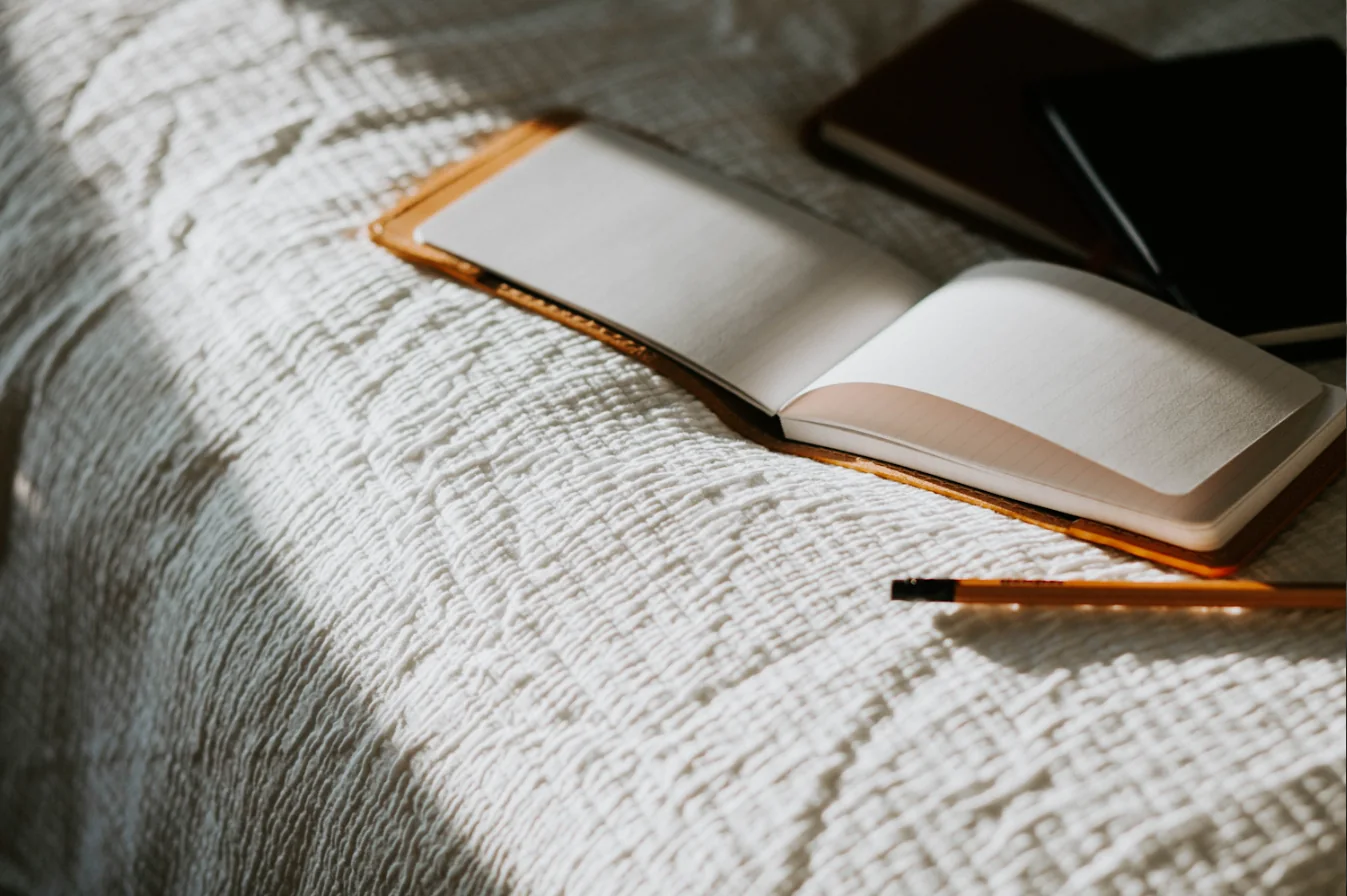 Carnet ouvert et crayon posés sur un couvre-lit blanc