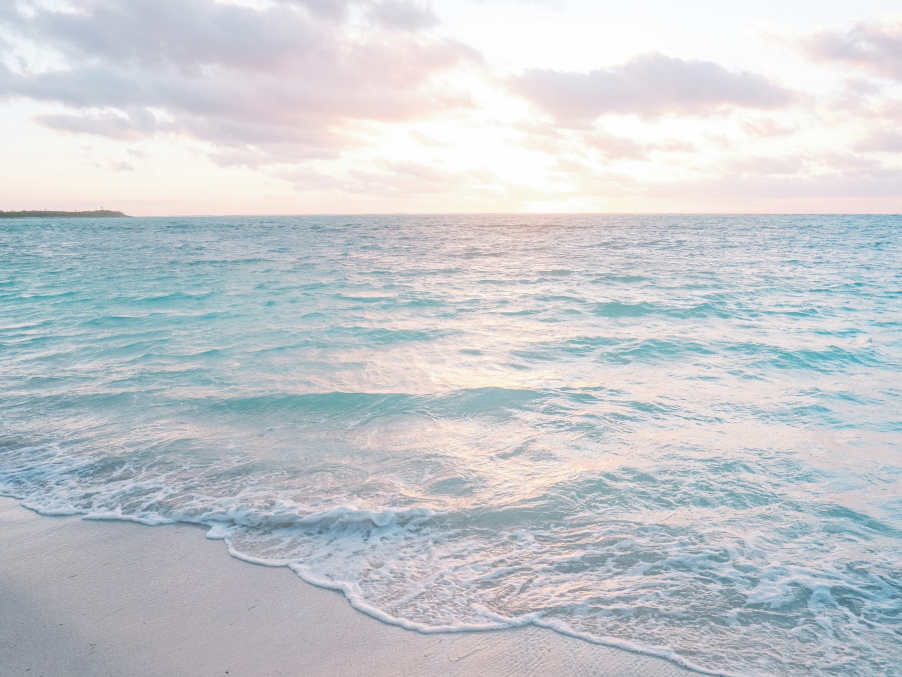 Calm ocean and white sand under a pale pink morning sky