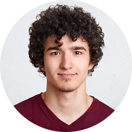 Young man with curly dark hair and light facial hair wearing a maroon shirt, facing forward with a neutral expression.