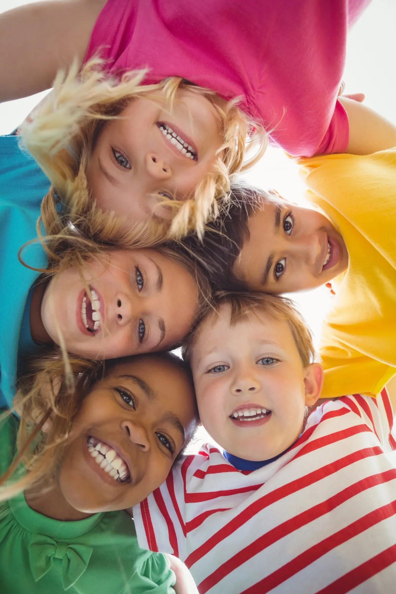 Five smiling children with their heads together, looking up at the camera