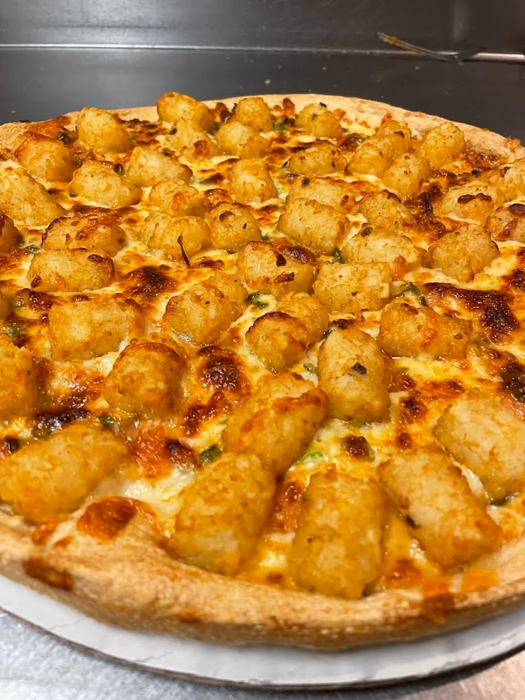 Pizza topped with melted cheese and numerous golden brown tater tots evenly spread on the crust.