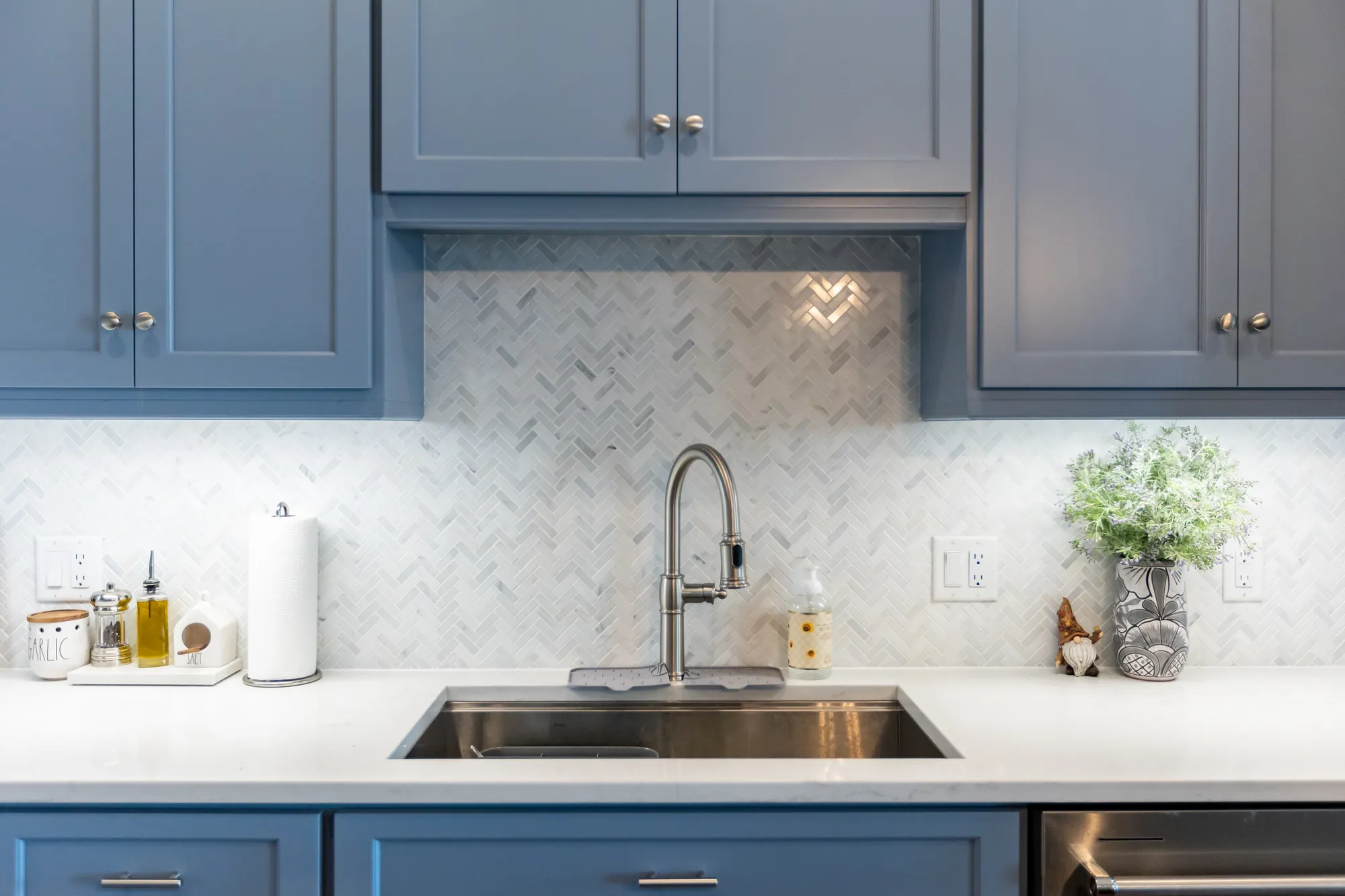 Blue painted shaker cabinets with a herringbone tile backsplash
