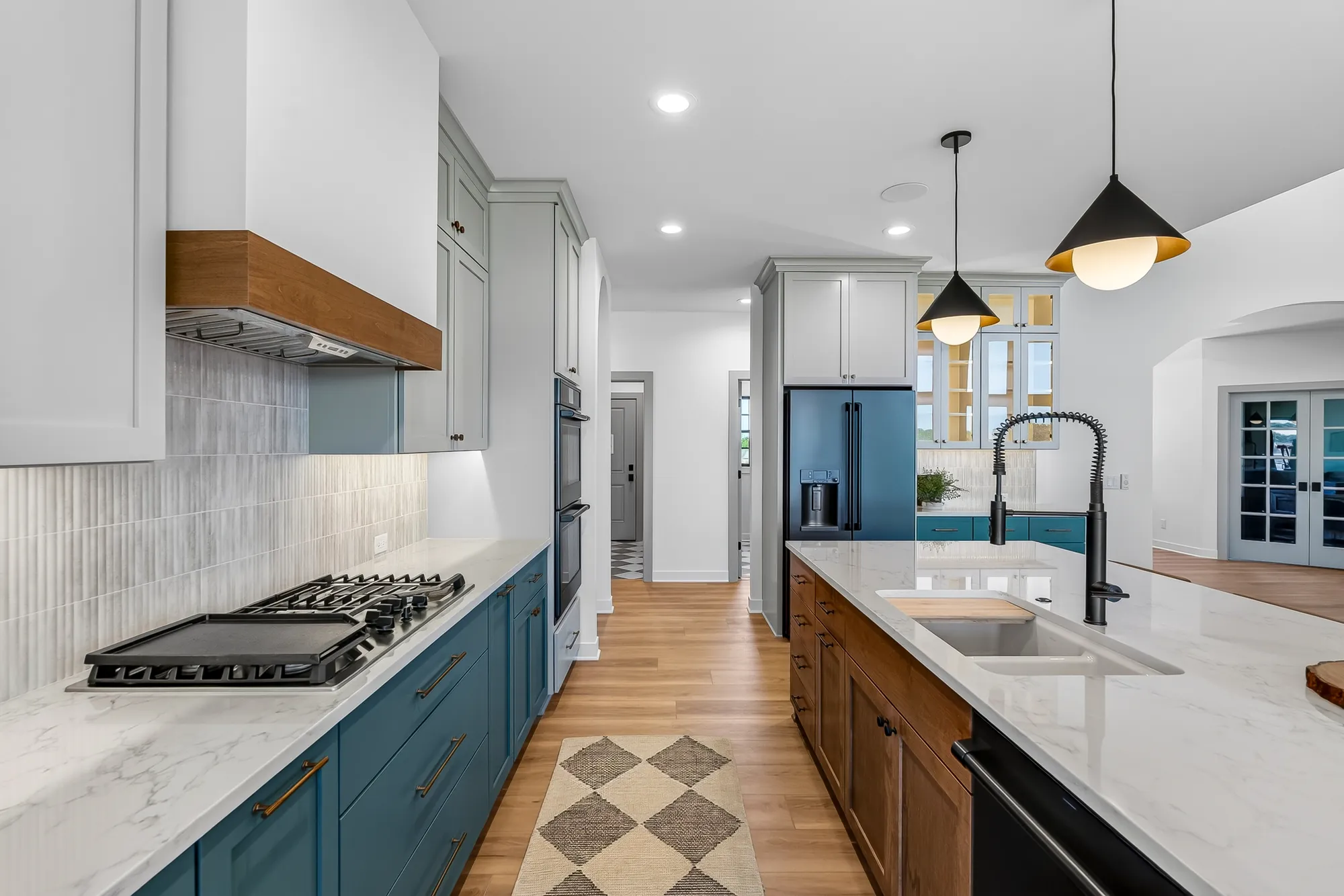 New-construction kitchen with teal lower cabinets, a wood hood and a quartz island