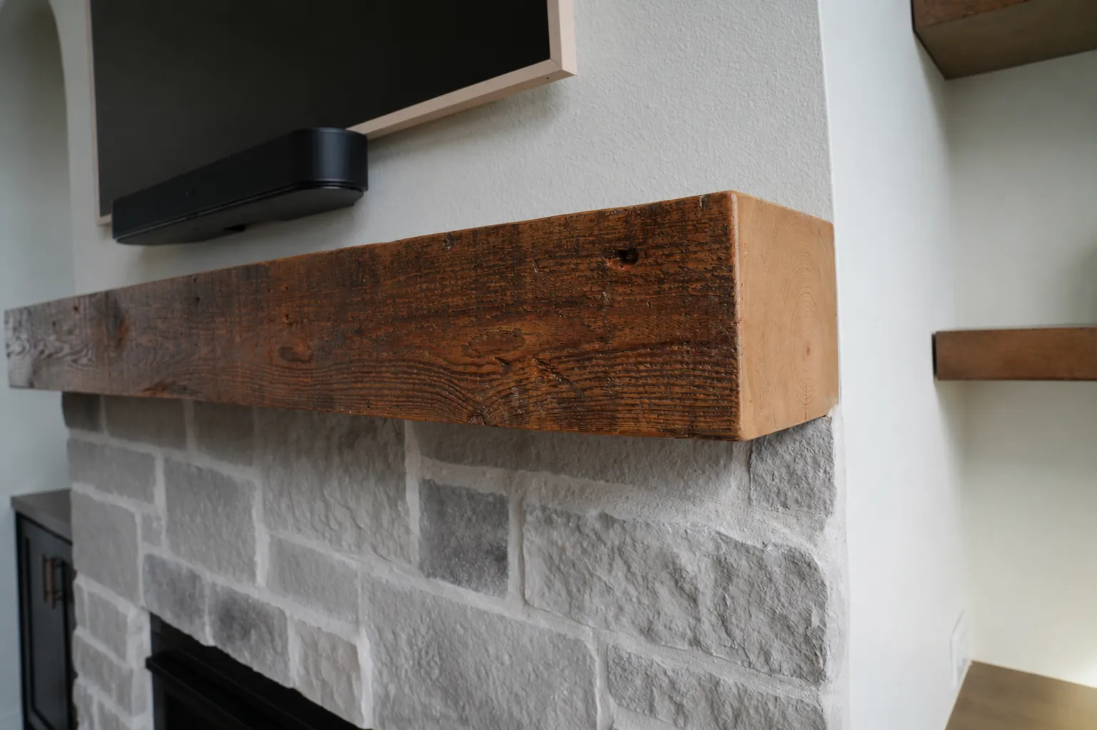 Rustic wood beam fireplace mantel over a stone surround