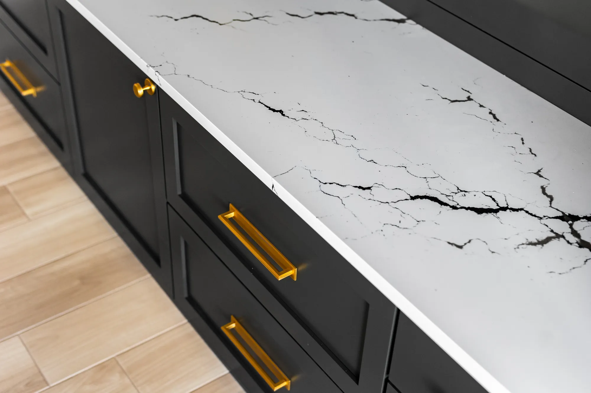 Close-up of a white quartz countertop edge over black cabinets with brass pulls