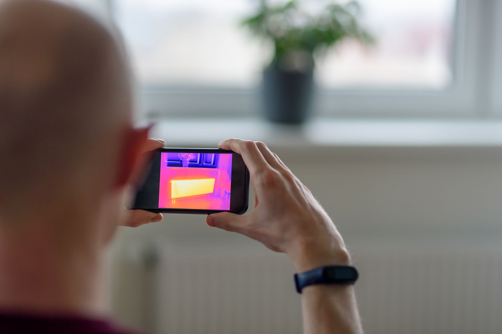 Energy auditor using a thermal imaging camera to find heat loss in a building